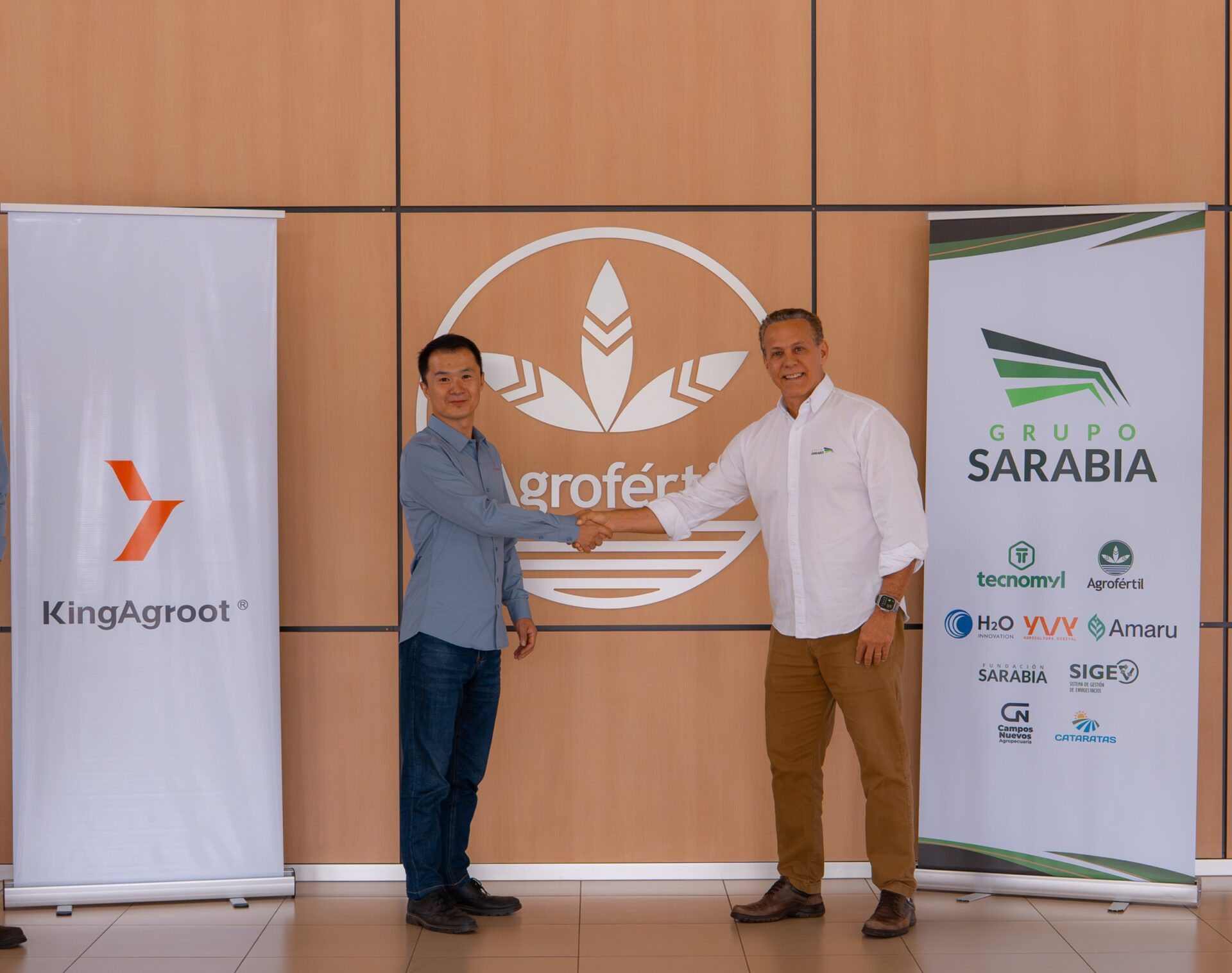 Paulo Sarabia y un representante de KingAgroot se saludan frente al emblema de Agrofértil